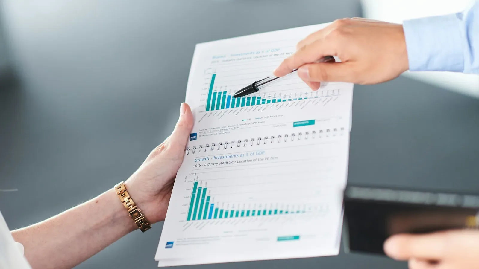 Two people analyzing a document with green bar charts.