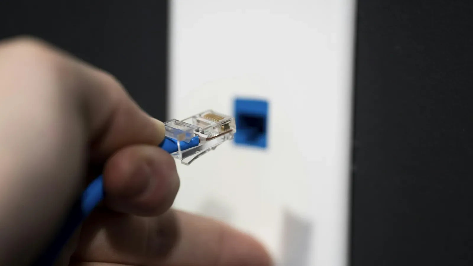 Hand connecting an Ethernet cable to a network wall socket.