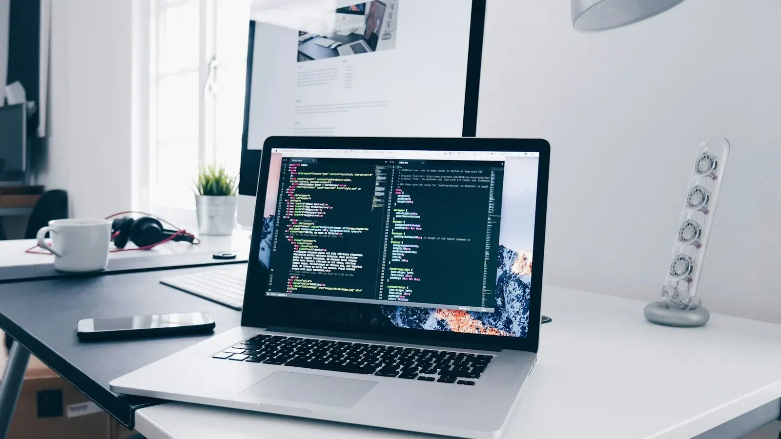 A MacBook with lines of code on its screen on a busy desk.