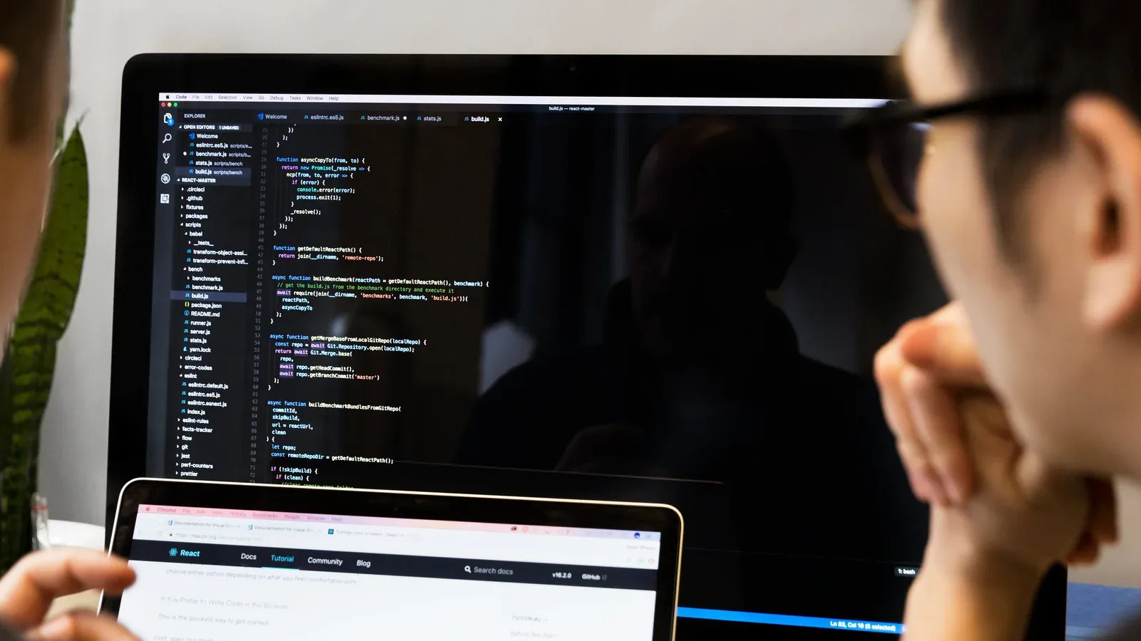 Developer reviewing JavaScript code across a monitor and laptop.