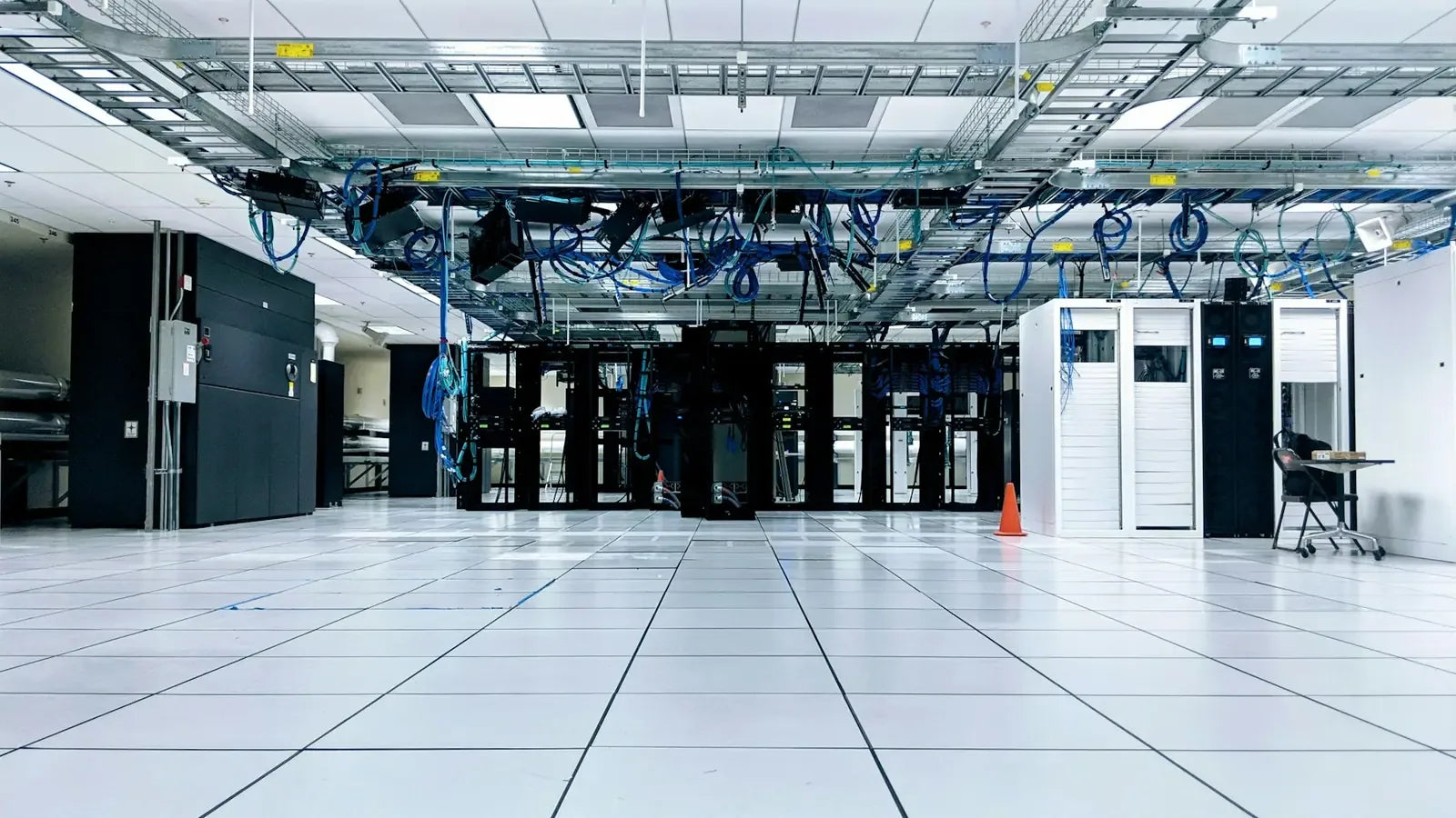 A server room with rows of black and white cabinets under blue cables.