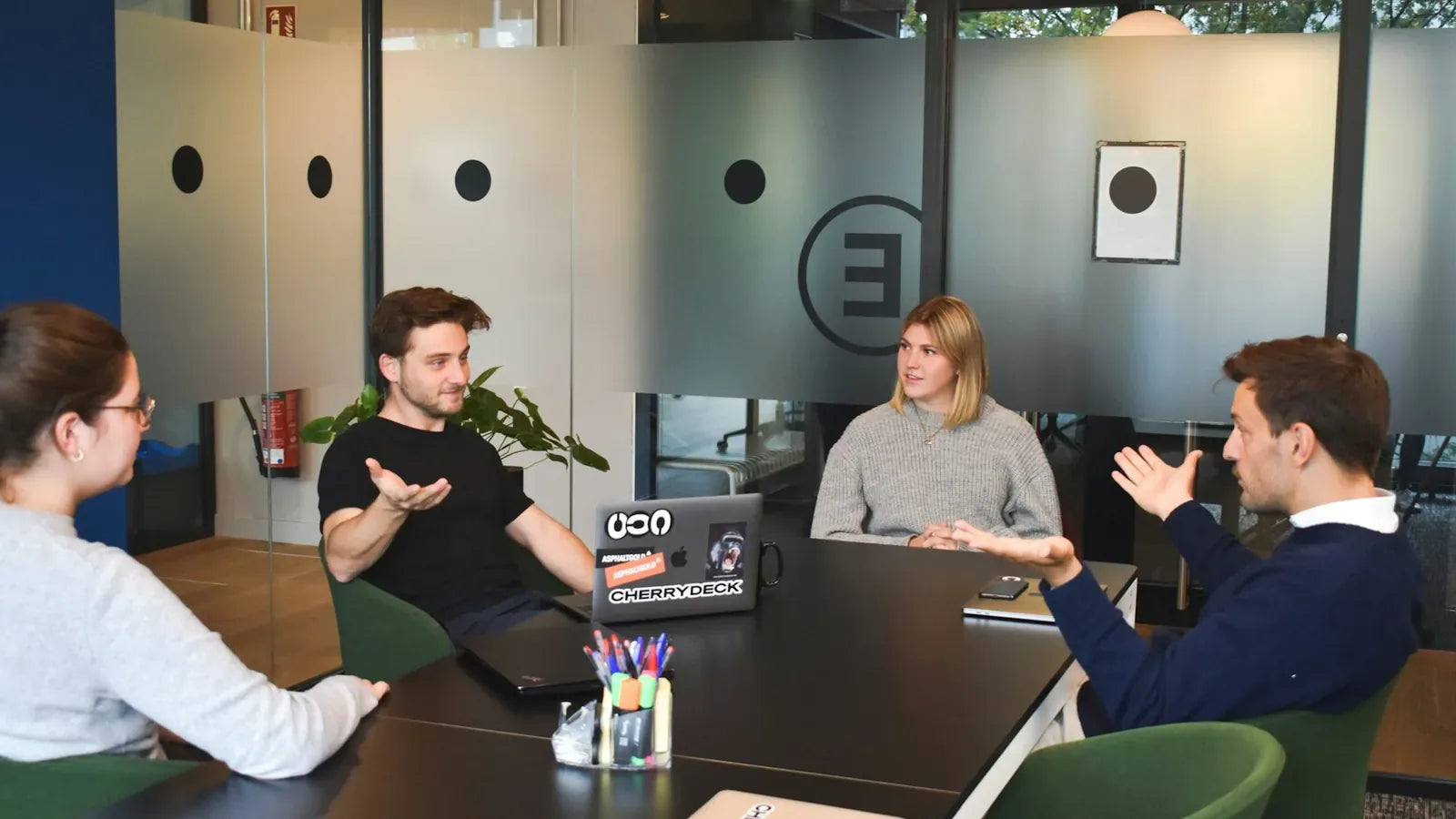 Four people in a meeting around a black table in a modern office.